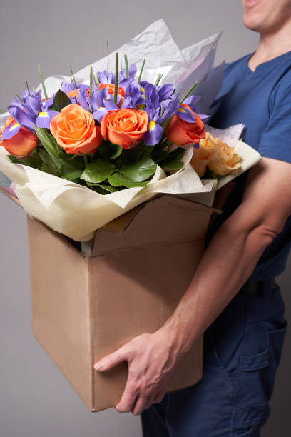 istock White male courier holding a large cardboard box with several bouquets 1322790947