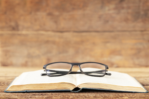 Back to school and education concept. A glasses on the open book on a wooden background and place for text.