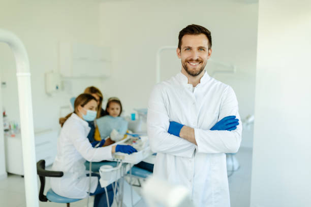 Male dentist standing with his hands crossed, wearing gloves and white coat and looking at camera. stock photo