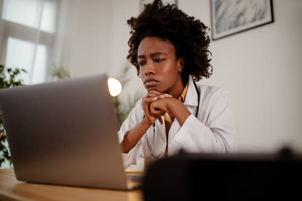 Displeased black healthcare worker using computer and reading an e-mail at doctor's office. stock photo