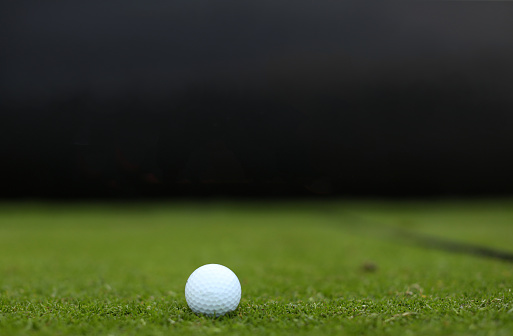 A white golf ball on a manicured tee box with a dark background on an unrecognizable golf course in South Africa.