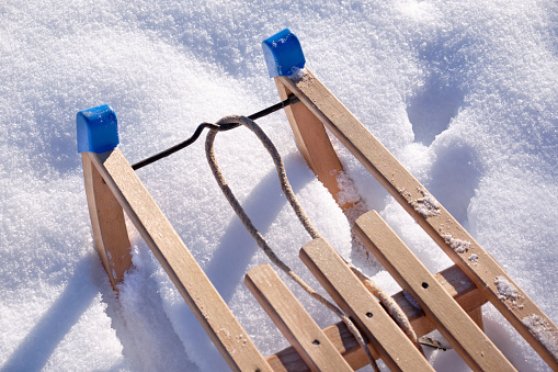 Close-up of a wooden sledge standing in pure white snow on a sunny winter day. Seen in Germany in February.