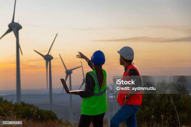 Young Maintenance Engineer Team Working In Wind Turbine Farm At Sunset Stock Photo - Download Image Now