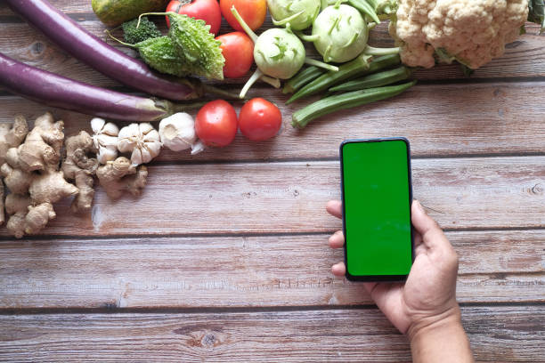 istock fresh vegetables and holding mart phone with green screen on table 1322807911