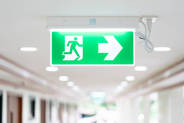 ein pfeil-lichtkasten-schild von emergency fire exit wird an der decke in krankenhaus gehweg, idee für event-feuer oder evakuierungsübungen aufgehängt. - late light stock-fotos und bilder