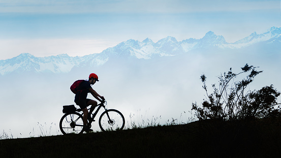 A cyclist riding uphill with misty Southern Alps in the background