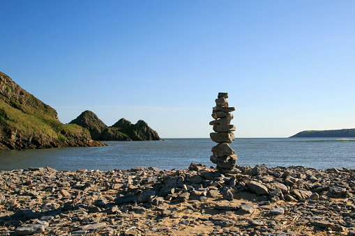 Zen stones stacked on a beach with Three Cliffs Bay in the background - Gower