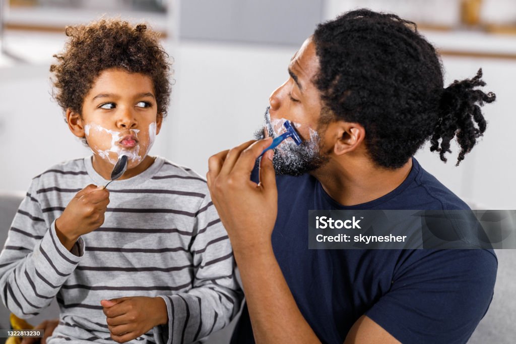 I am shaving just like my dad! African American single father teaching his small son how to shave at home. Shaving Stock Photo