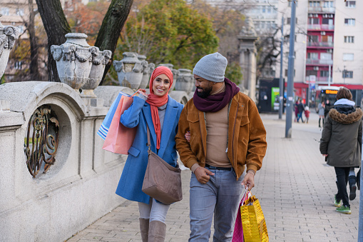 Young Couple of Different Ethnicities is Walking with Paper Bags Down the City Streets After Visiting Shopping Mall.