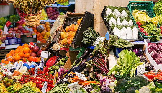 A large variety of healthy fruits and vegetables at a market stall, with lettuce, zucchini, cherry tomatoes, eggplants, artichokes, fennel, kale, broccoli, oranges and apples. The labels tag indicates the product and the price in Italian language. The traditional Mediterranean diet consists of natural, healthy and fresh products, including fruits, vegetables and grains. Image in high definition format.