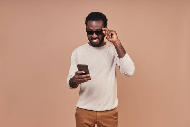 istock Handsome young African man in casual clothing using smart phone and smiling 1322820598