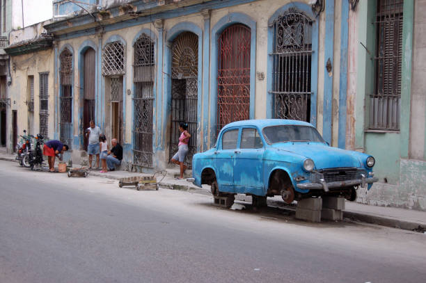 Havana, Cuba - November 19, 2005:  Street scene in Central Havana as a mechanic repairs a motorbike in the road with a battered vintage car resting on bricks.