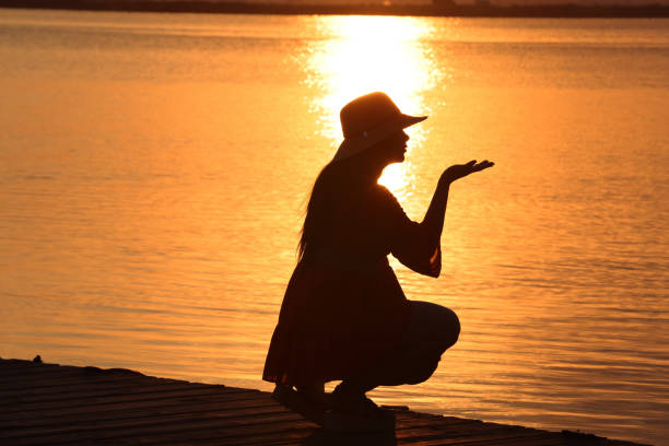 Silhouette of young lady at sunset looking across a lake. High resolution 45Mp using Canon EOS R5 with associate lenses