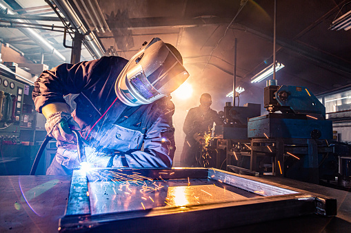 The two handymen performing welding and grinding at their workplace in the workshop, while the sparks 