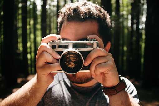 A young man taking a picture with a vintage film camera inside a forest