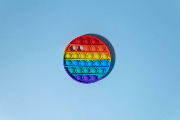istock An anti-stress, square rainbow-colored toy pop it on a blue background. There is a place for your text. Simple dimple. The child will play. shadow. 1322824199