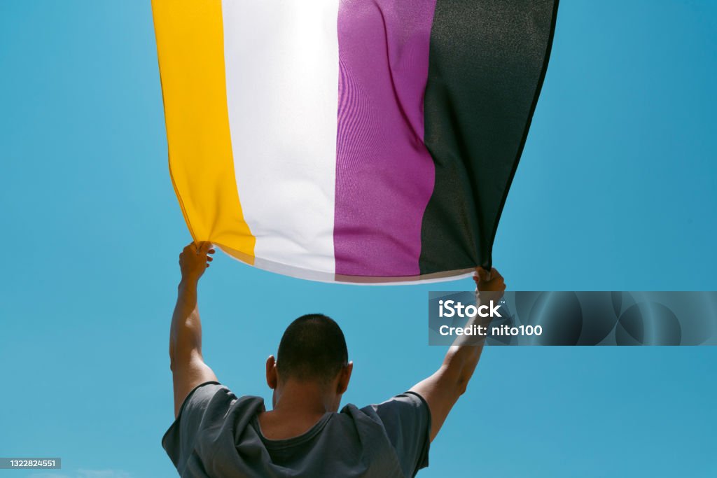 person waving a non-binary pride flag closeup of a young caucasian person, seen from behind and below, waving a non-binary pride flag on the sky Non-Binary Gender Stock Photo