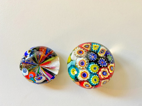 High angle closeup view of two beautiful, round Venetian glass paperweights with colorful patterns on a light background