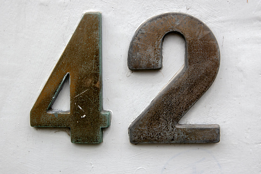 Weathered grunge square metal enameled plate of number of street address with number 57 closeup
