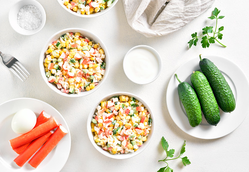 Russian style imitation crab salad with crab sticks, corn, eggs, cucumber and rice. White background, top view, flat lay