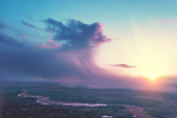 Magical dramatic sunset in the countryside in spring with the dramatic stormy sky. Rural landscape in the evening. Aerial view of brook, village, and arable fields. Panoramic view