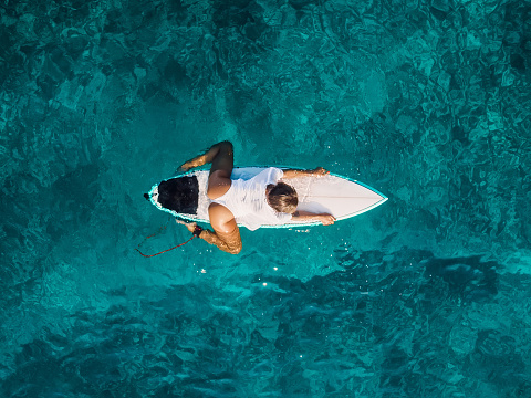Attractive surf girl relaxing on surfboard in transparent ocean. Aerial view with surfer woman