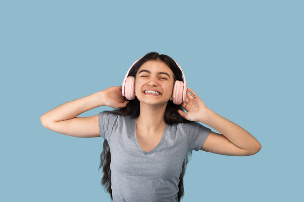 felice adolescente indiano in moderne cuffie wireless godendo di canzoni popolari nell'app audio, ascoltando musica - indian girls audio foto e immagini stock