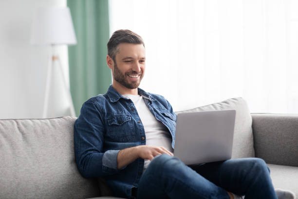 uomo sorridente che usa il laptop, ha un lavoro part-time a casa - people cheerful happiness candid foto e immagini stock