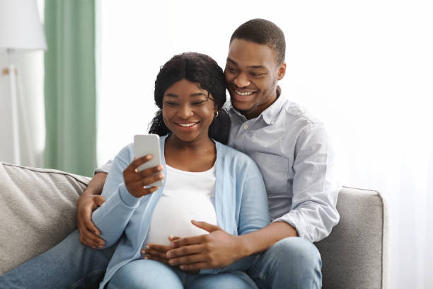 istock Cheerful pregnant african american couple using mobile phone 1322838529