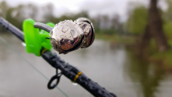 Silver fishing bells are worn on a fishing rod while fishing. Bite-call signal, at the tip of the rod. A bite alarm will alert you to a bite. Fishing tackle close-up