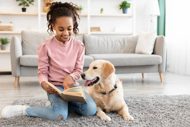 giovane ragazza afro che legge libro con cane a casa - dog education holding animal foto e immagini stock