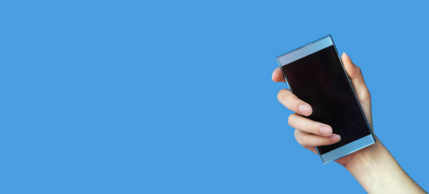 istock Woman's hand holds mobile phone with blank screen on blue isolated background. Concept mockup for your ad. Close-up, copy space, banner 1322841614