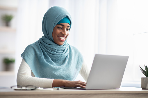 Job Opportunities For Muslim Women. Portrait Of Smiling Black Islamic Woman In Hijab Working On Laptop In Office, Religious African Lady In Headscarf Sitting At Desk And Using Computer, Copy Space