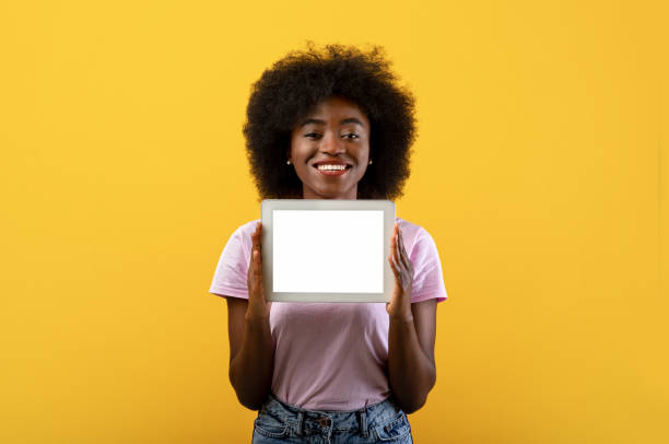 istock Joyful african american lady holding digital tablet with blank screen over yellow background 1322842604