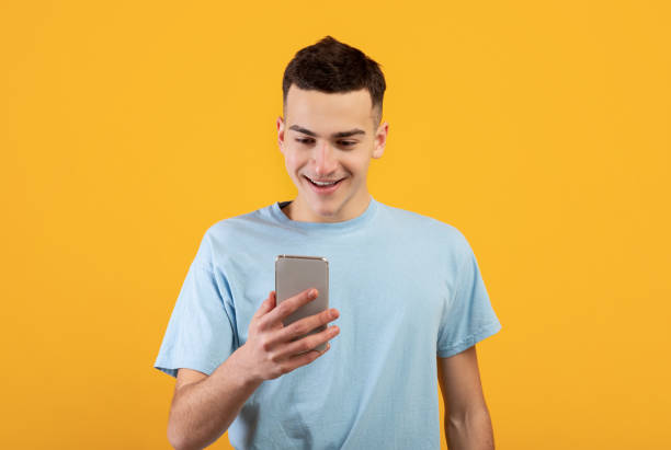 istock Cheerful young man using mobile phone, chatting online, having business meeting or webinar on orange background 1322843004
