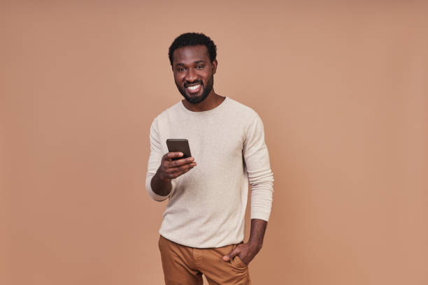Handsome young African man in casual clothing using smart phone and smiling