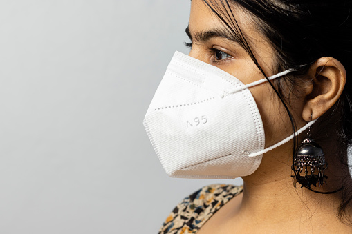 Close up side face of an Indian woman wearing N 95 mask on white background