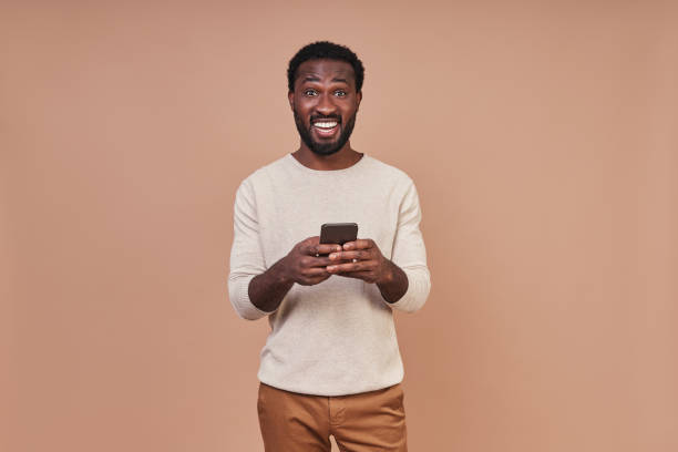 istock Handsome young African man in casual clothing using smart phone and smiling 1322843184