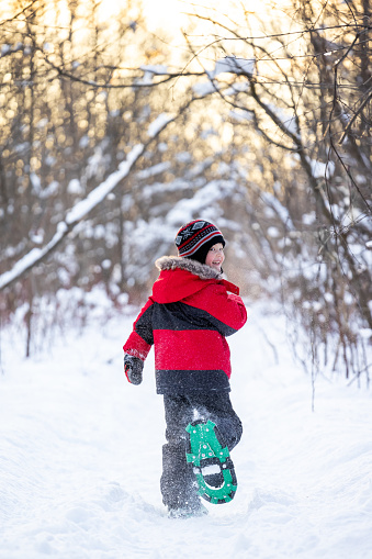 Little Boy Snowshoeing and running in Powder Snow Outdoors in Winter during sunset.