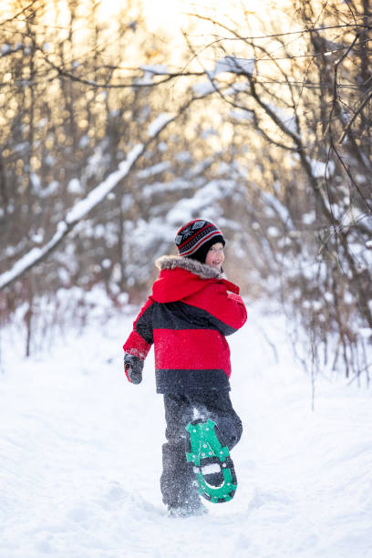 Little Boy Snowshoeing in Powder Snow Outdoors in Winter during sunset stock photo