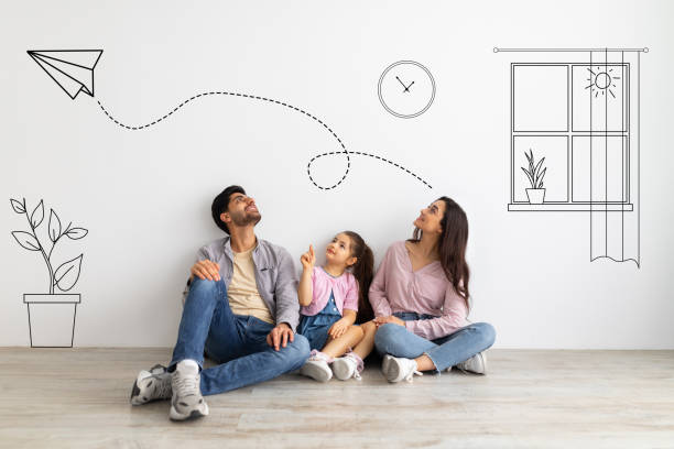 Lovely child girl and her young parents dreaming about their new home with sketch interior drawings against white wall Lovely child girl and her young parents dreaming about their new home with sketch interior drawings against white wall, collage with illustrations on background. Family sitting on floor family photo on wall stock pictures, royalty-free photos & images