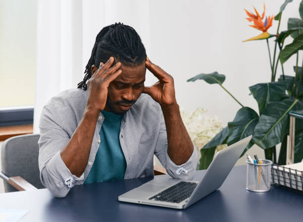 istock Remote work from home. African American man works at home workplace using laptop gets stress from distance work and lack of communication with people 1322844492