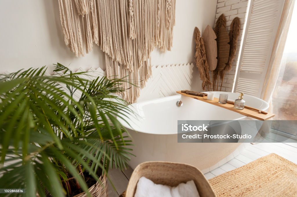 Cozy bathroom interior with big bathtub, plant and rustic decoration Cozy bathroom interior background with big white bathtub, natural green plant and rustic decoration elements. Light spacious bathing room background with no people for apartment design advertisement Bathtub Stock Photo