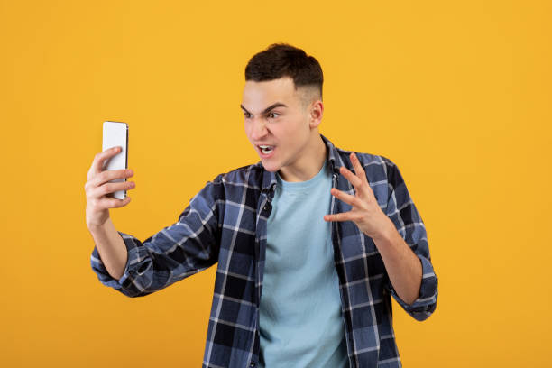 istock Terrible connection. Angry millennial man looking at his smartphone in rage over orange studio background 1322845609