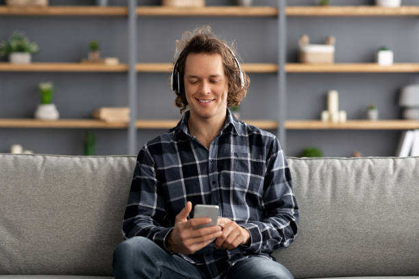 istock Relaxed Guy Wearing Headphones Using Mobile Phone Sitting At Home 1322845764