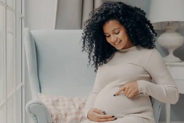Photo of Future african american mother in white dress talking with baby inside belly