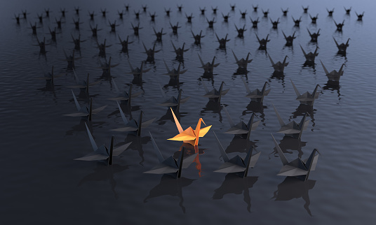 Standing out from the crowd concept with an orange colored paper crane between the black ones on the water. ( 3d render )