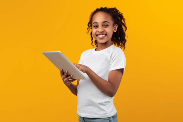 istock Black girl standing with tablet at yellow studio 1322847154