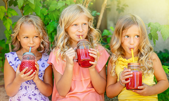 Three Caucasian girls drinking watermelon smoothie outdoors. Summertime leisure concept.