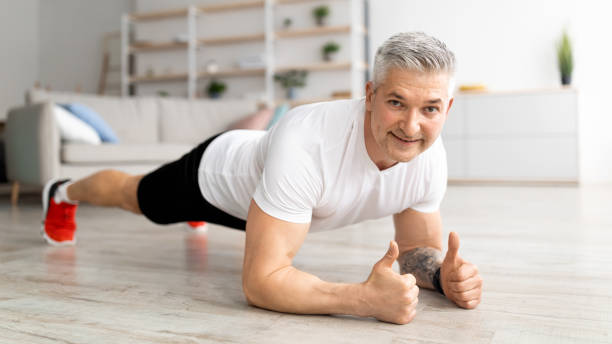 entraînement domestique. homme mature sportif debout dans la planche du coude et renforçant les muscles des abdos, faisant de l’entraînement physique - core workout photos et images de collection